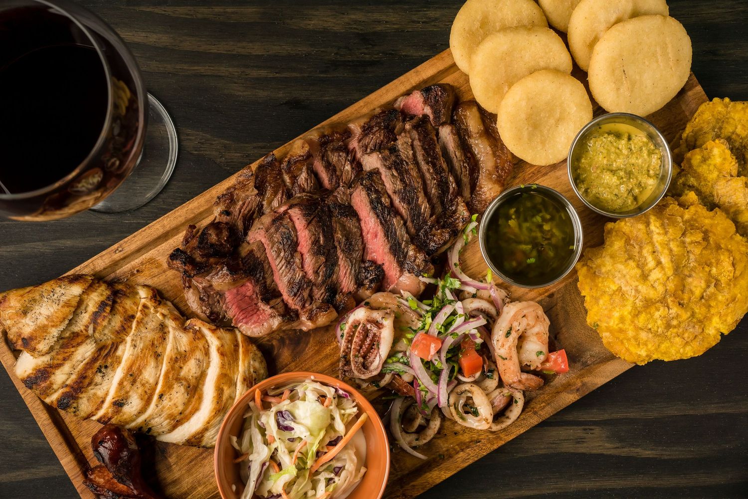 Gourmet charcuterie board with grilled meat, sauces, bread and sides on wooden serving platter.