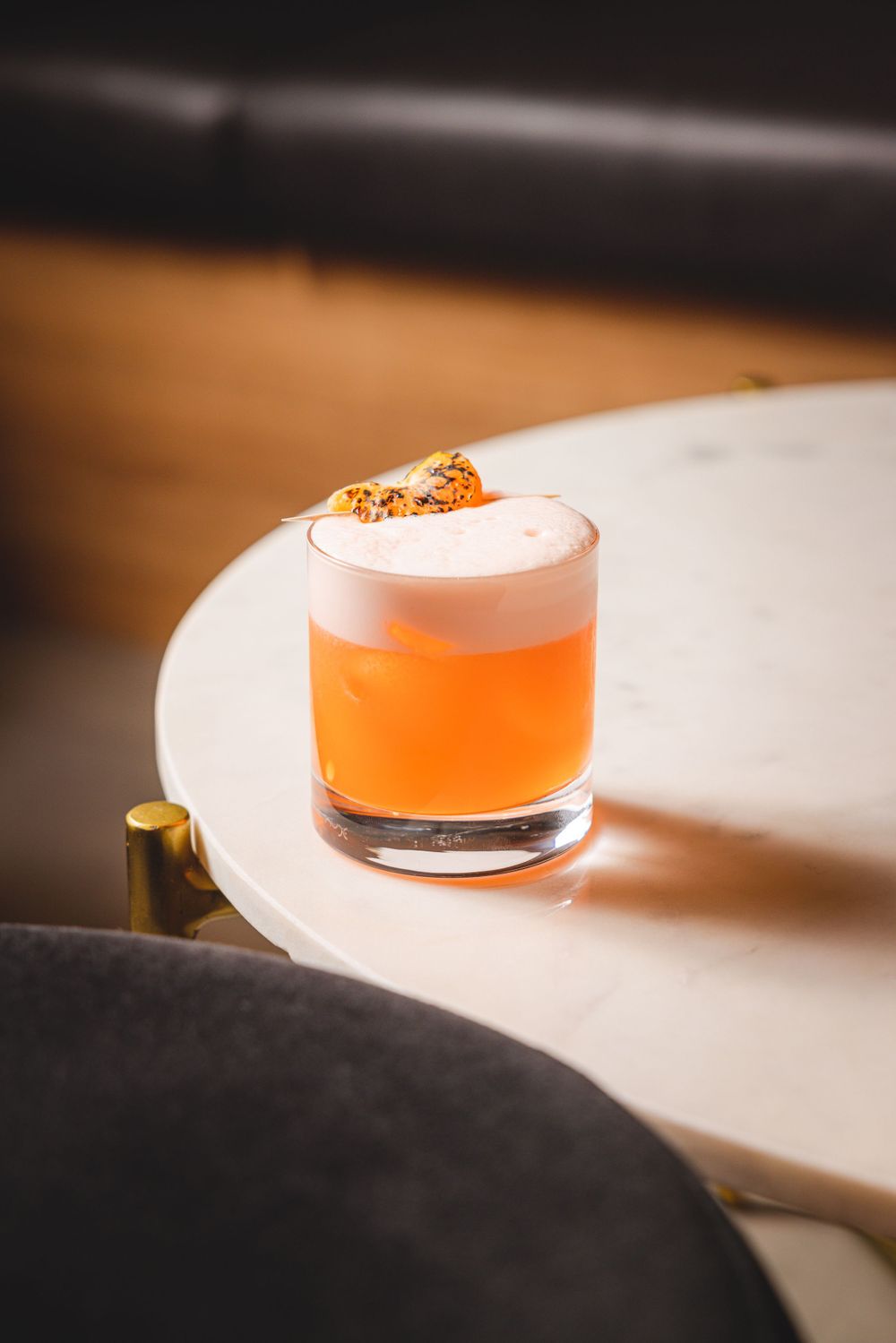 Orange cocktail with foam topping and garnish served in a rocks glass on a white surface.