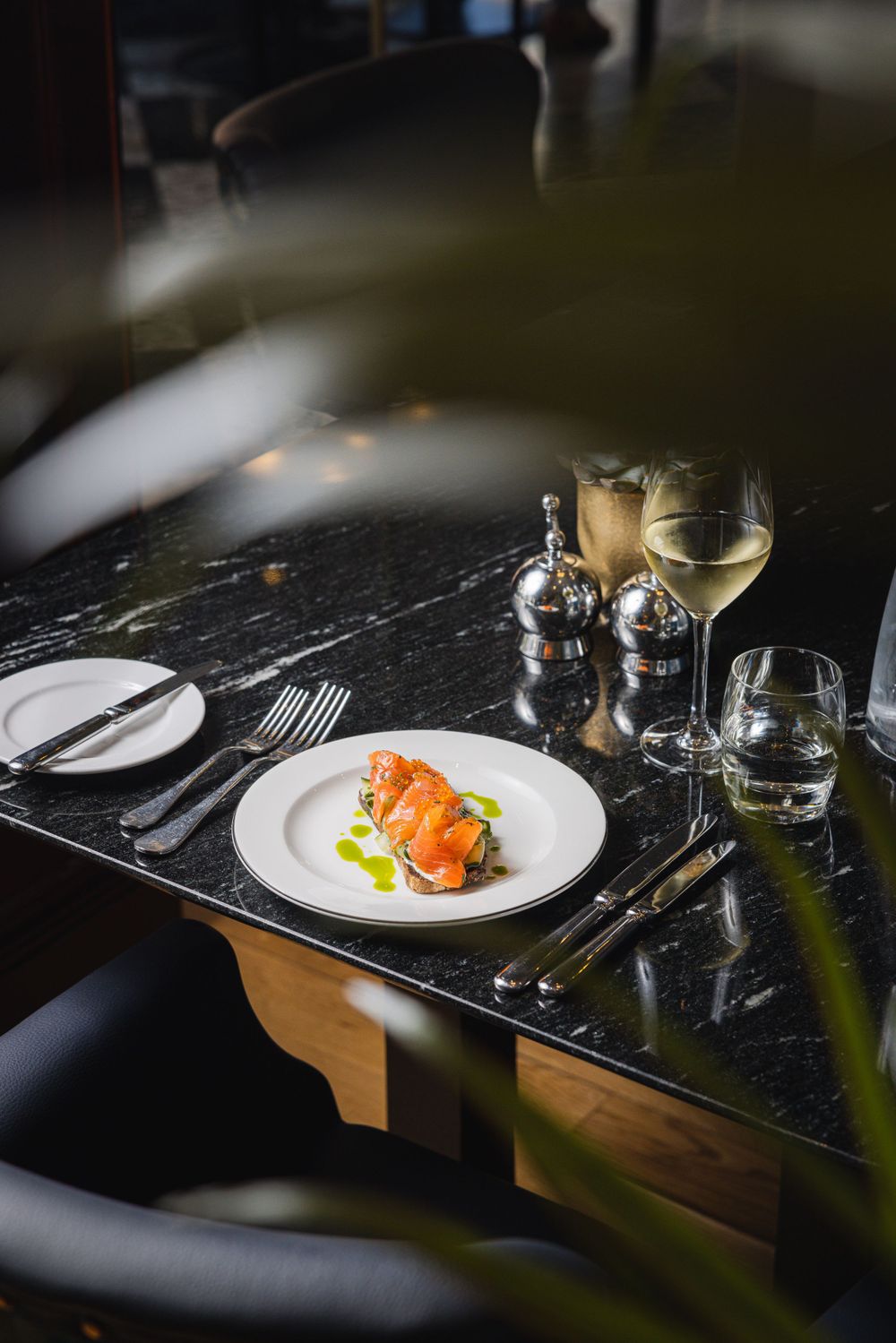 Elegant plated seafood dish with white wine on a black marble table in moody restaurant lighting.