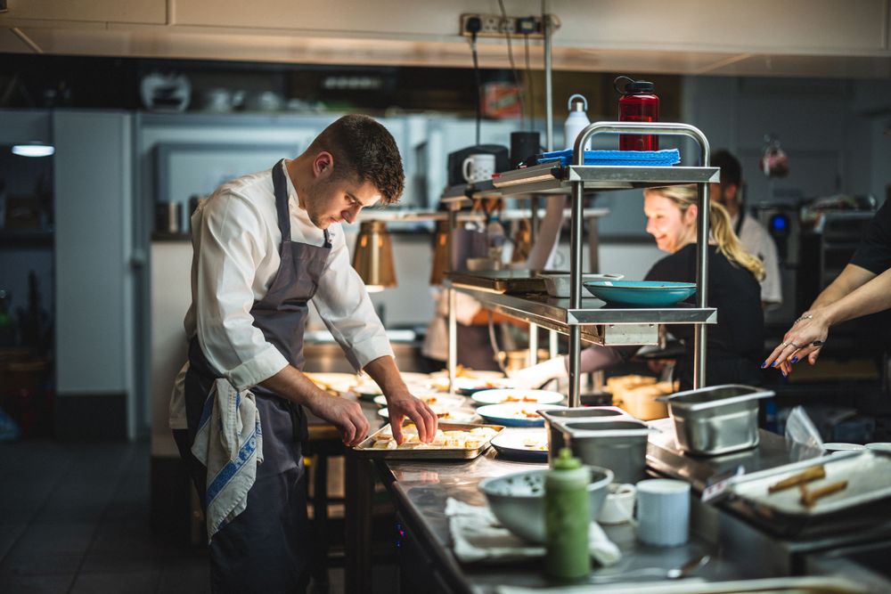 Chef preparing food at a commercial kitchen workstation with equipment and supplies.
