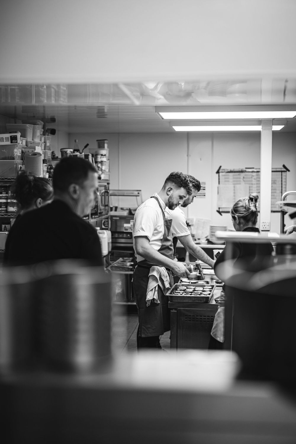 Kitchen staff working at prep station in commercial restaurant kitchen, shot in black and white.