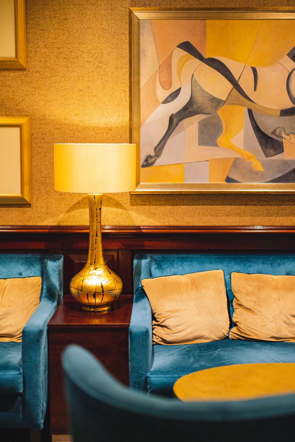 Mid-century modern lounge area with blue velvet chairs, gold lamp and abstract wall art.