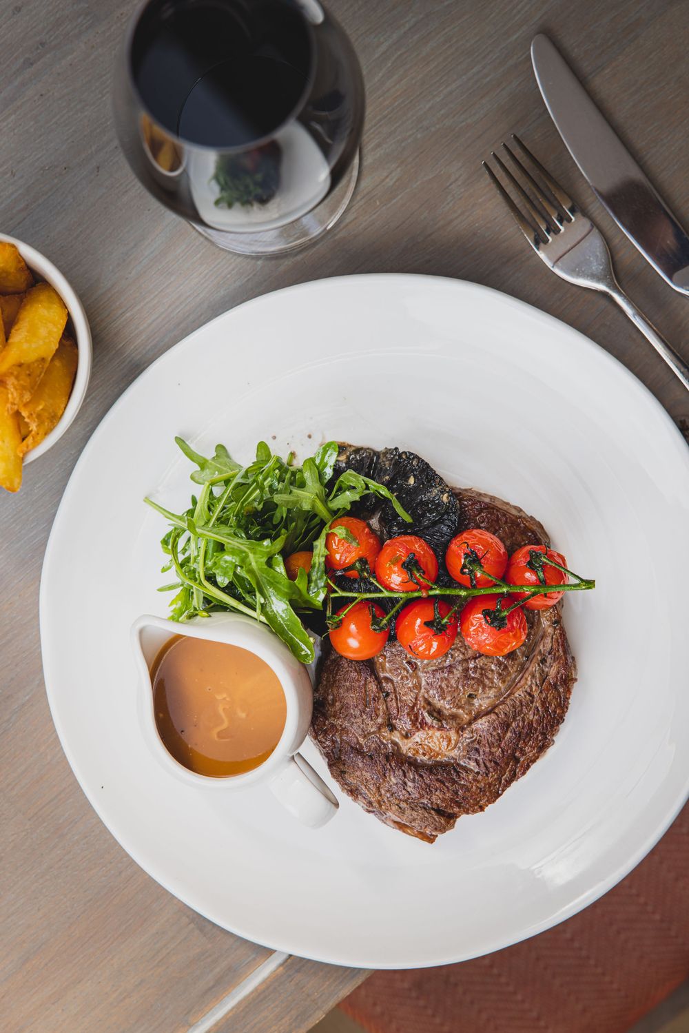 Steak dish with roasted tomatoes and arugula salad served with sauce.