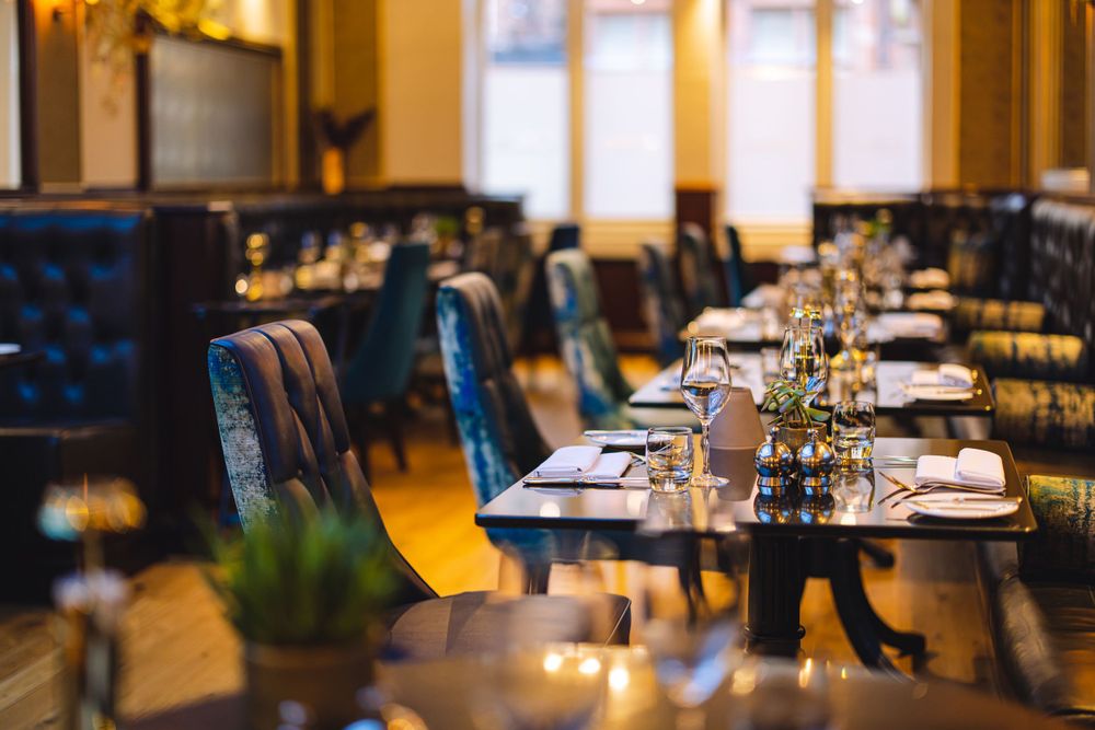 Elegant restaurant interior with blue velvet chairs and white tablecloths set for fine dining service.