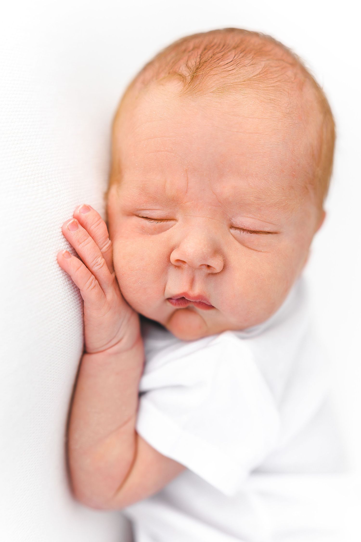 Peaceful sleeping newborn with hand resting on cheek against white background.