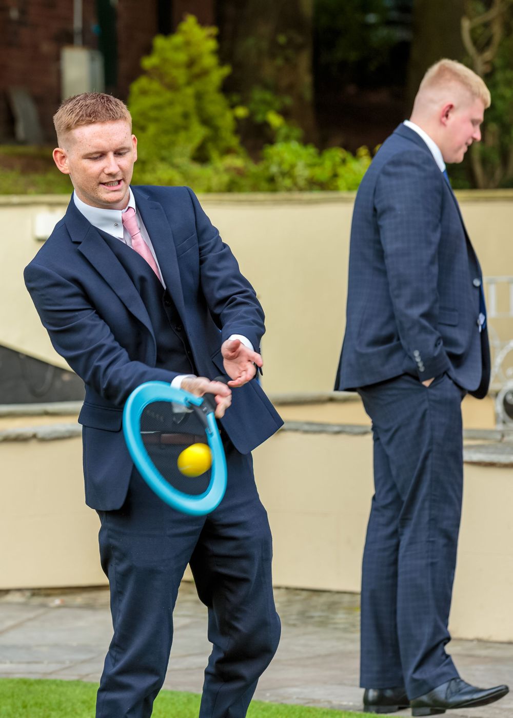 wedding guest in a smart suits hits the ball while playing tennis