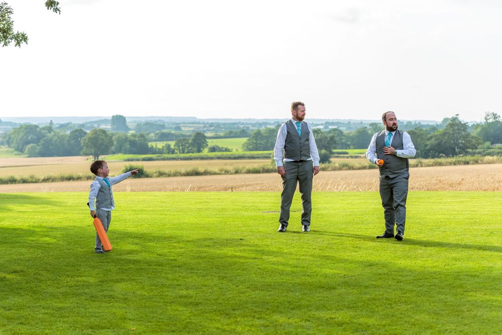 pageboy holding a cricket bat points to show the ushers where he hit the ball
