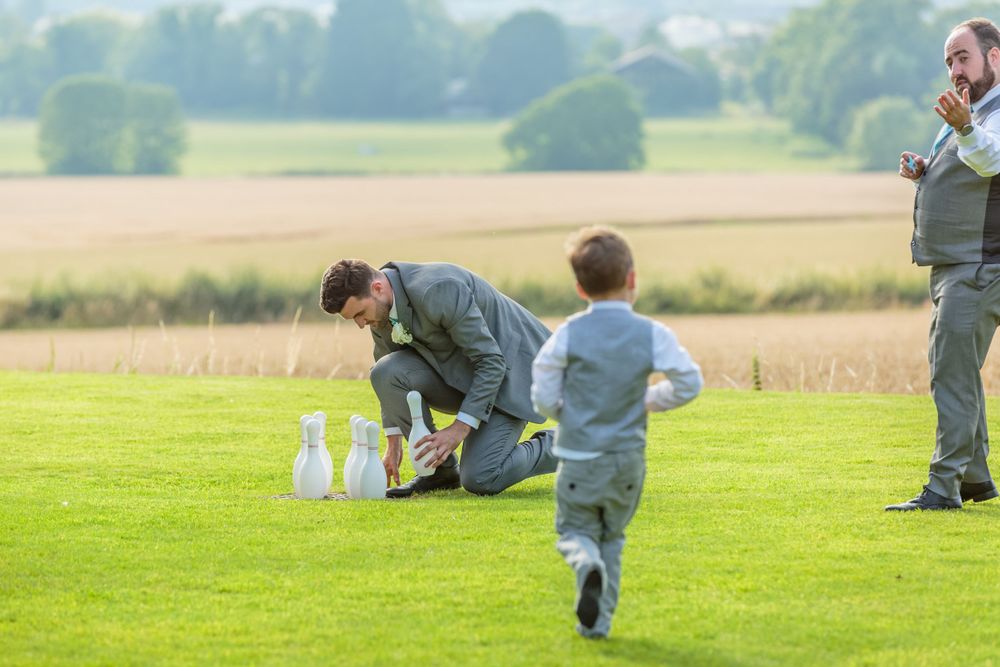 best man sets up the pins ready for a game of blowing with the page boy and an usher
