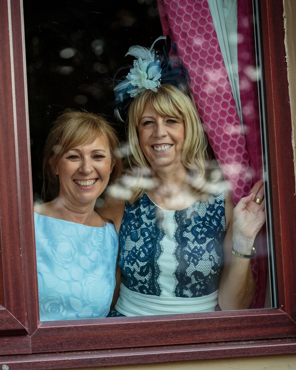 grooms mum and her friend smiling looking through their room window