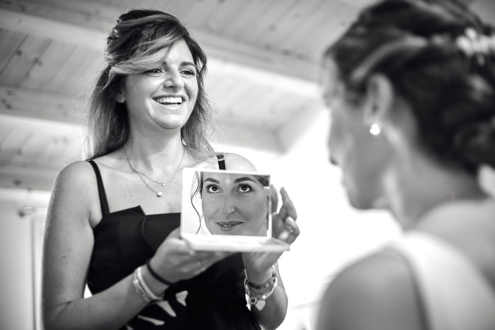 testimone di nozze tiene lo specchio alla sposa sorridendo surante i preparativi