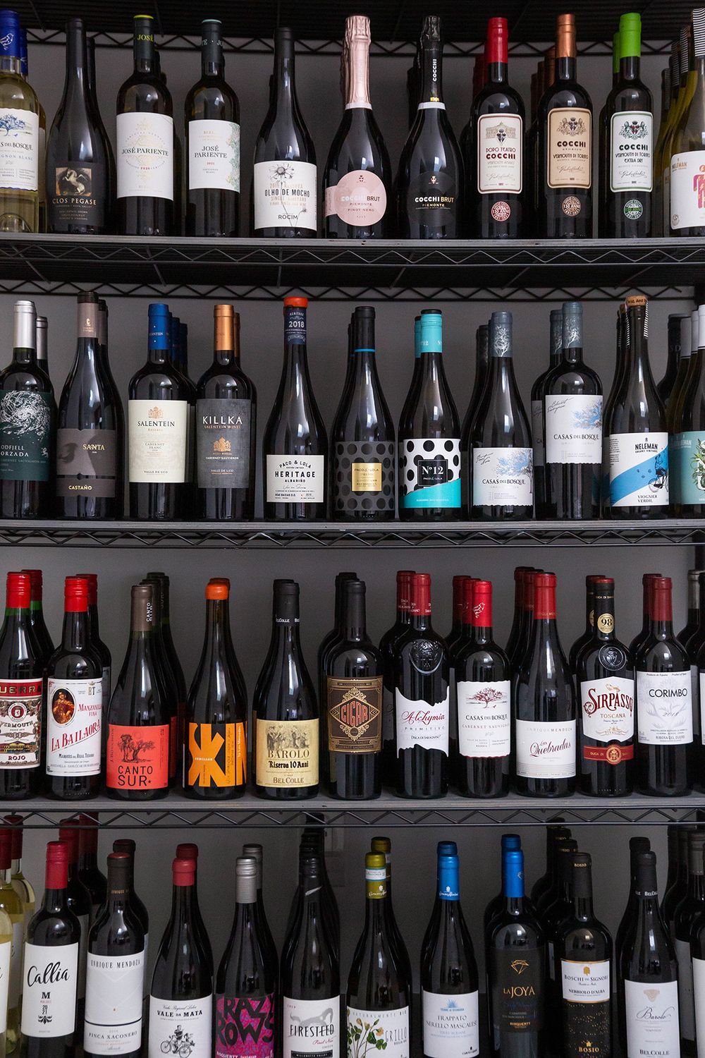 Multiple shelves displaying a diverse collection of wine bottles arranged in neat rows at a wine shop or bar.