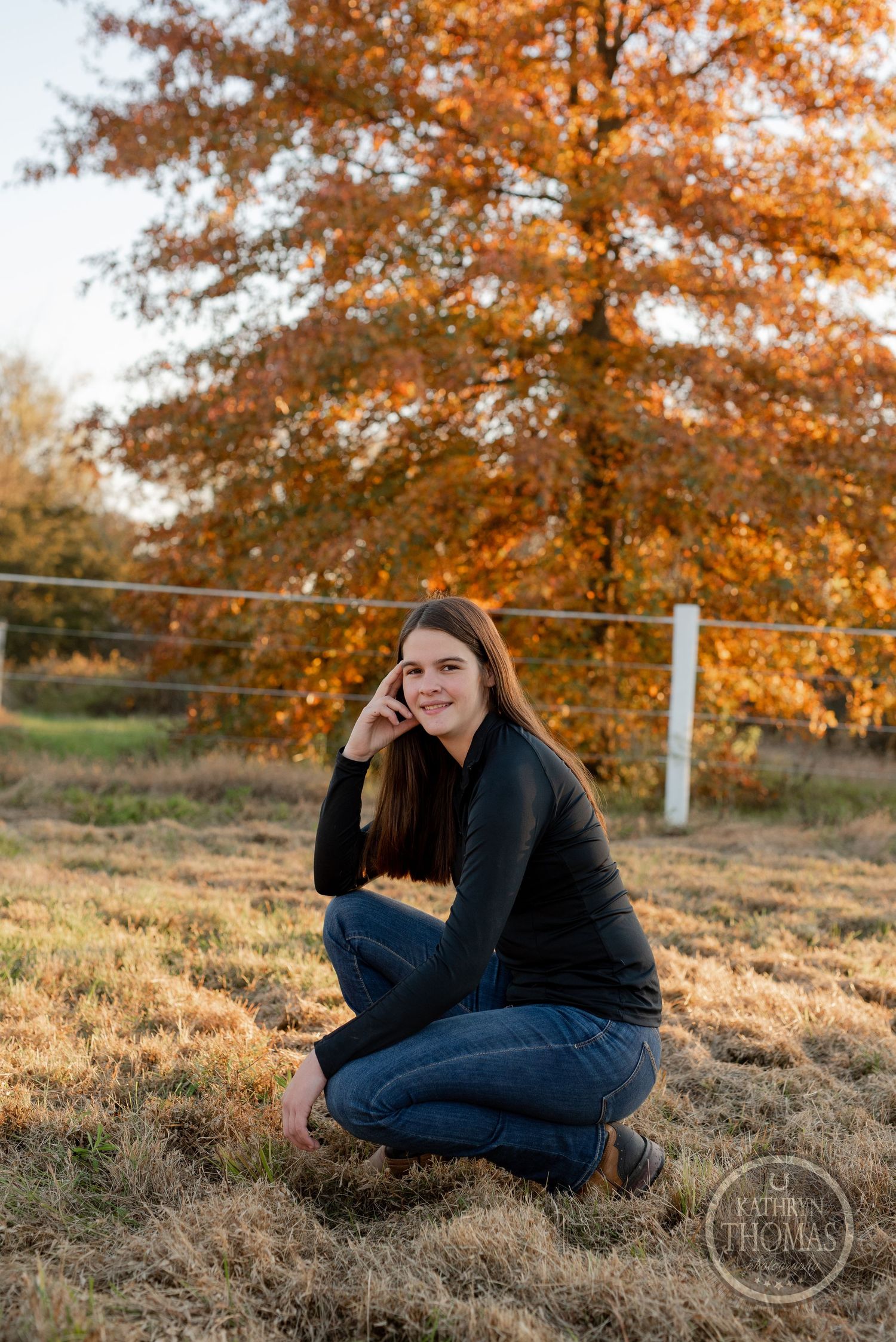 Autumn portrait in a rural field with orange foliage and a metal fence in the background.
