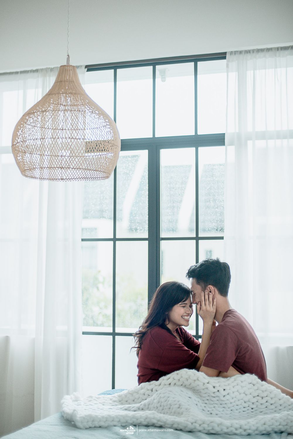 Romantic couple moment under woven pendant light by bright window with white curtains.