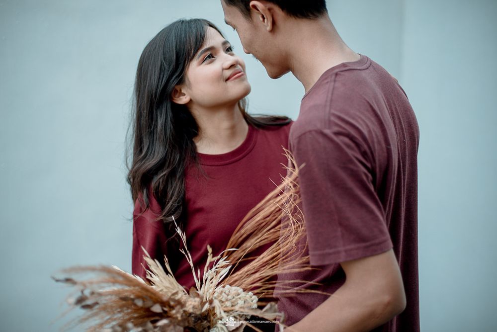 Couple in burgundy clothes sharing tender moment while holding dried flowers.