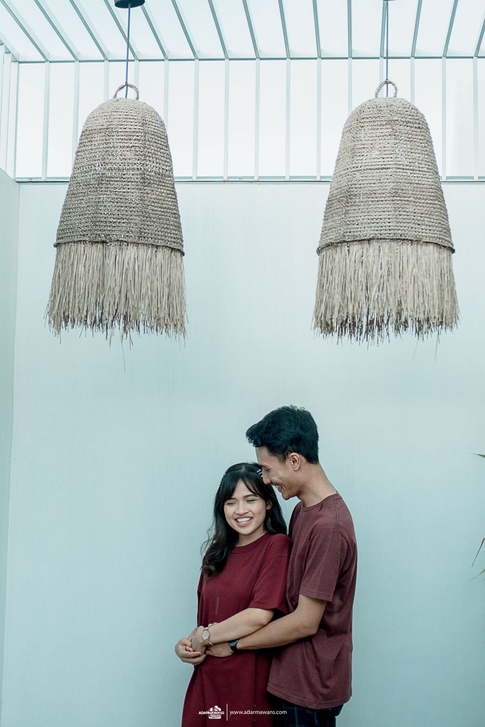 Intimate moment shared under hanging woven pendant lamps against a turquoise wall.