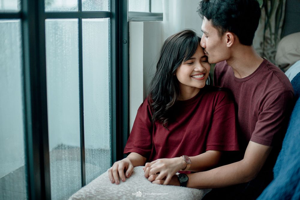Couple sharing an intimate moment by a window in matching burgundy tops.