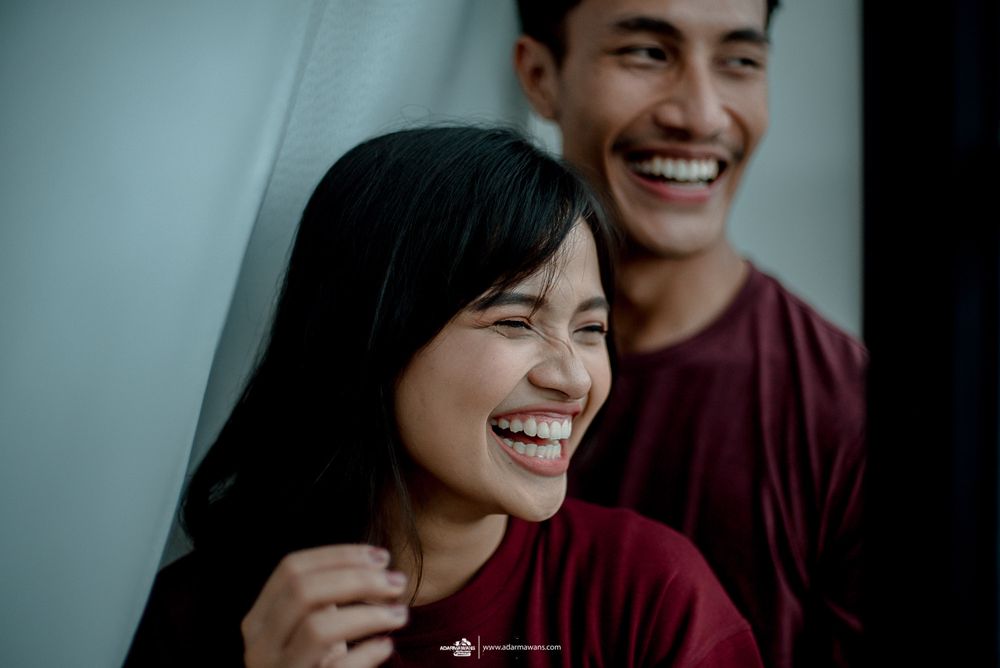 Couple in burgundy clothes sharing genuine laughter against a light wall.