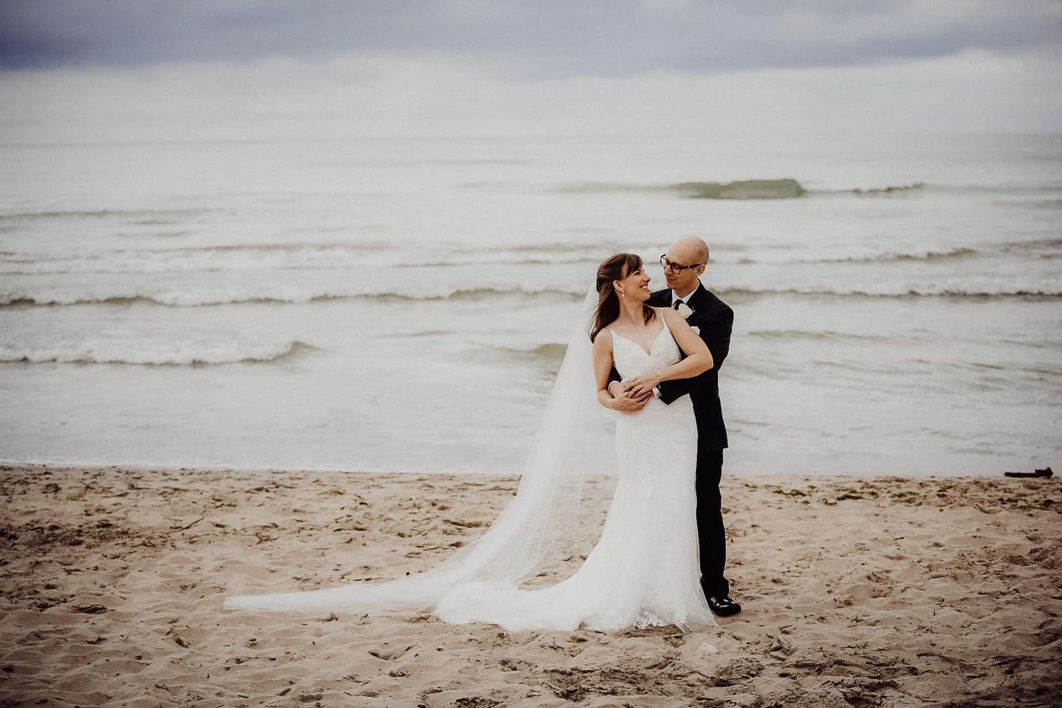 Romantic beach wedding photos of a couple embracing on the sandy shore at sunset.