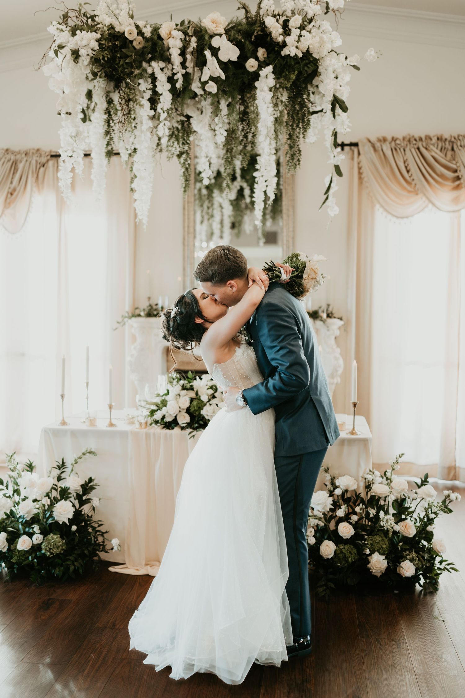 Romantic first dance under a stunning floral chandelier with white and green botanical decorations.