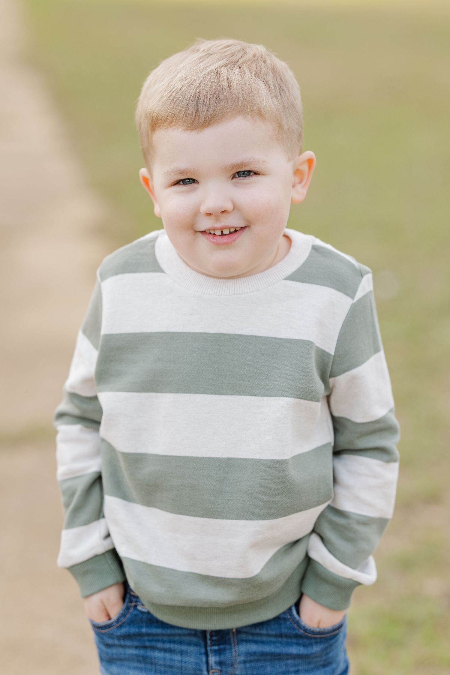 Young boy in striped sweater smiling at camera during outdoor portrait session.
