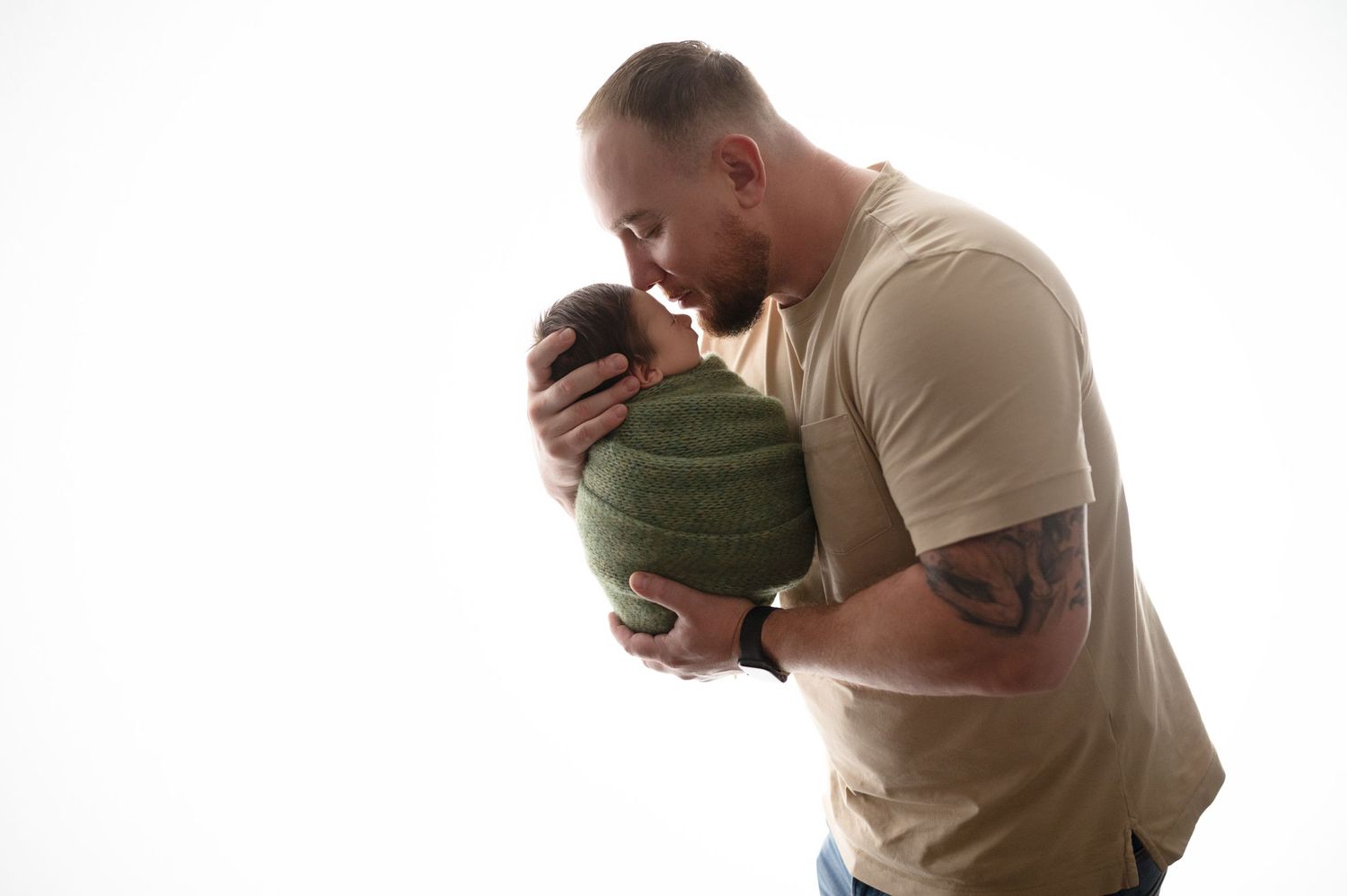 Father gazing lovingly at wrapped newborn in minimalist portrait.