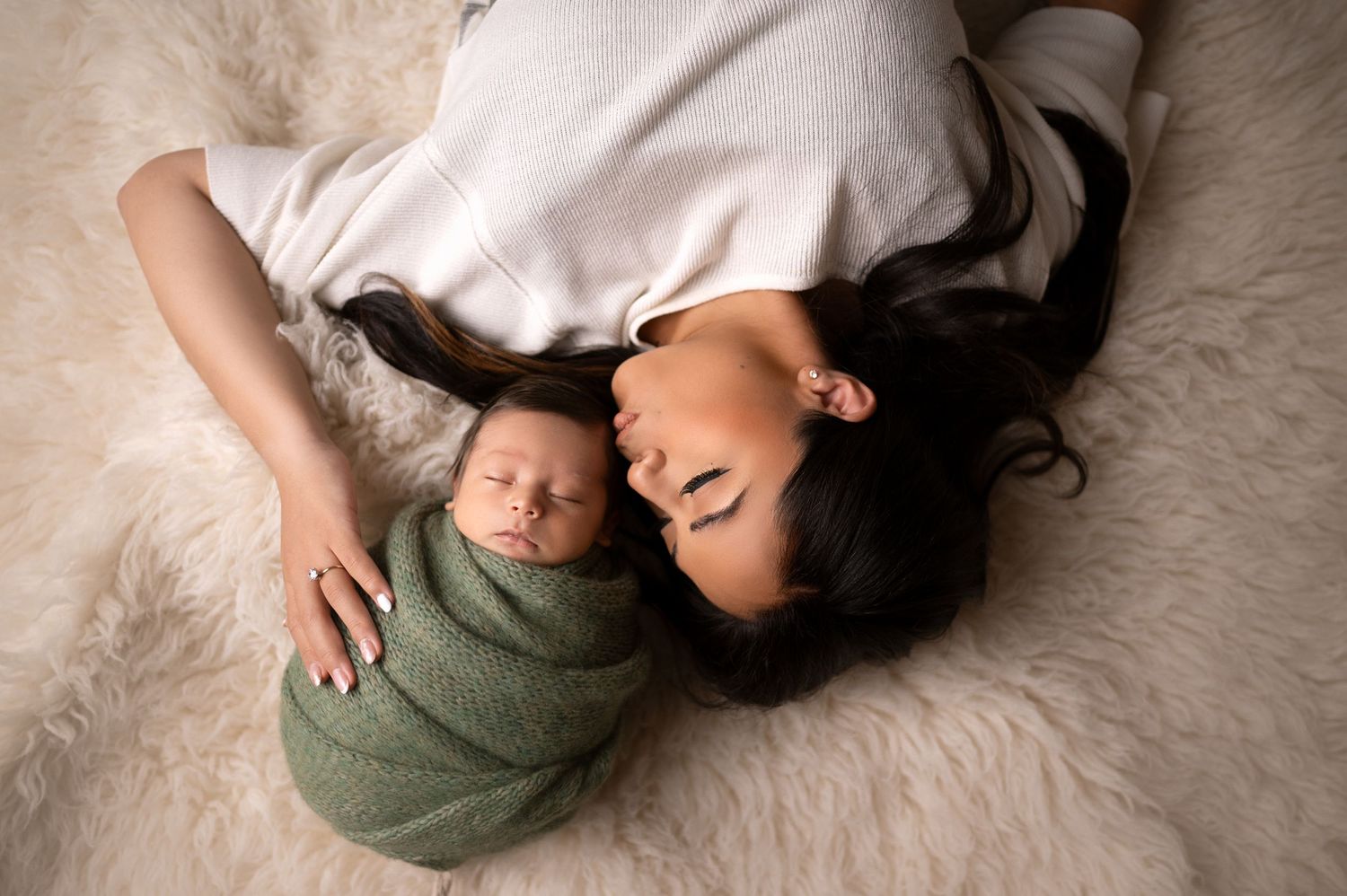 Overhead view of parent and baby wrapped in sage green sharing tender moment on white rug.