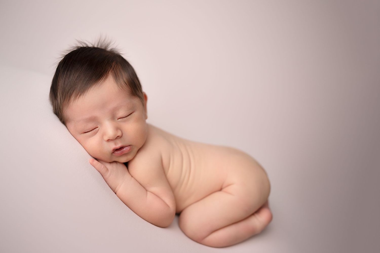 A sleeping newborn poses on pink backdrop in artistic nude portrait style.