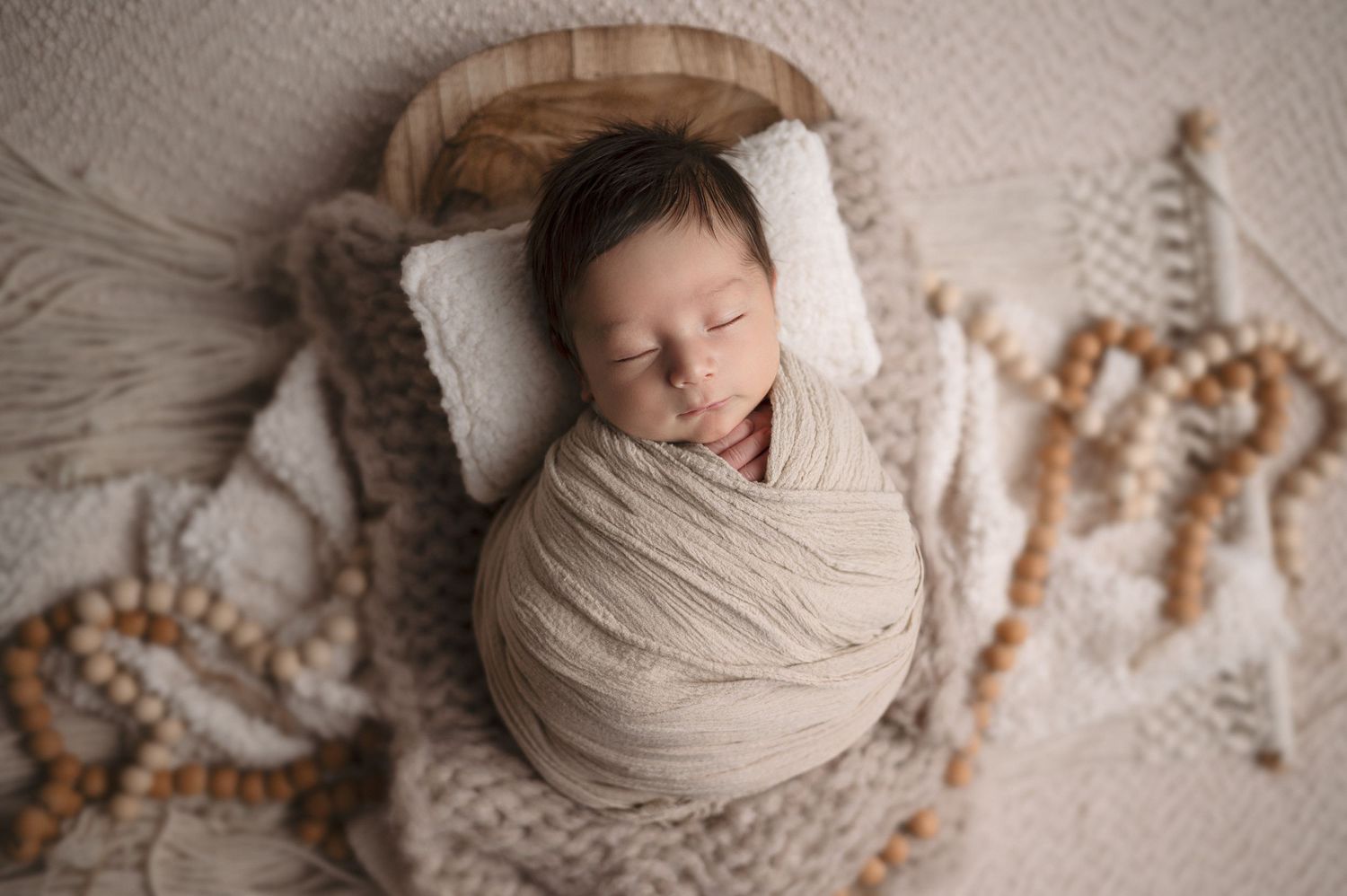 A peaceful newborn sleeps wrapped in beige fabric on textured bedding.