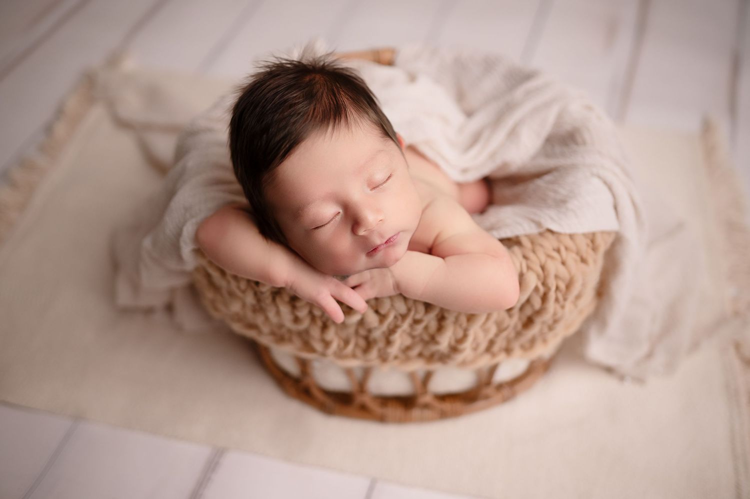 Sleeping baby nestled in woven basket with cream-colored bedding.
