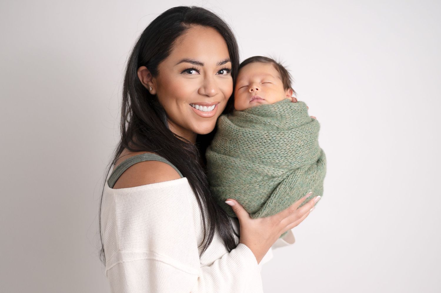 Natural light studio portraits capture authentic family connections with newborn in green swaddle.