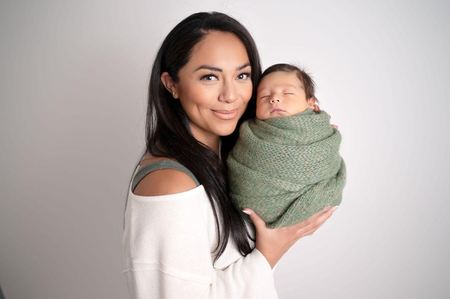 Professional studio photography showcases loving family moments with swaddled newborn.