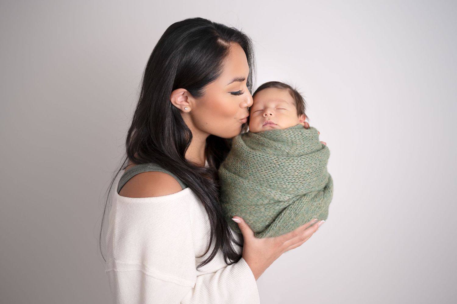 Mother cradling swaddled newborn in green wrap against white background.
