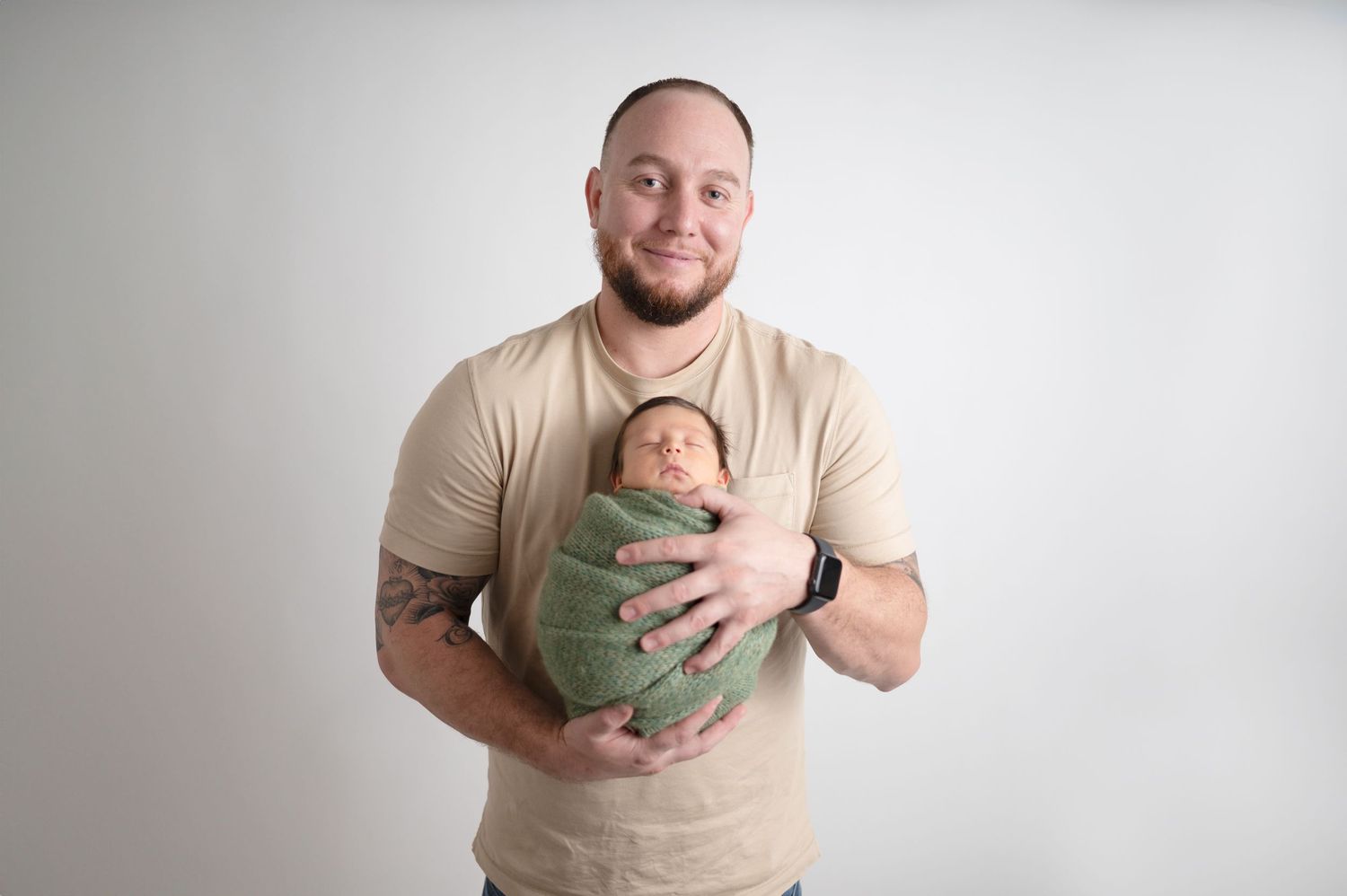 Father holding swaddled newborn in green wrap against white background.