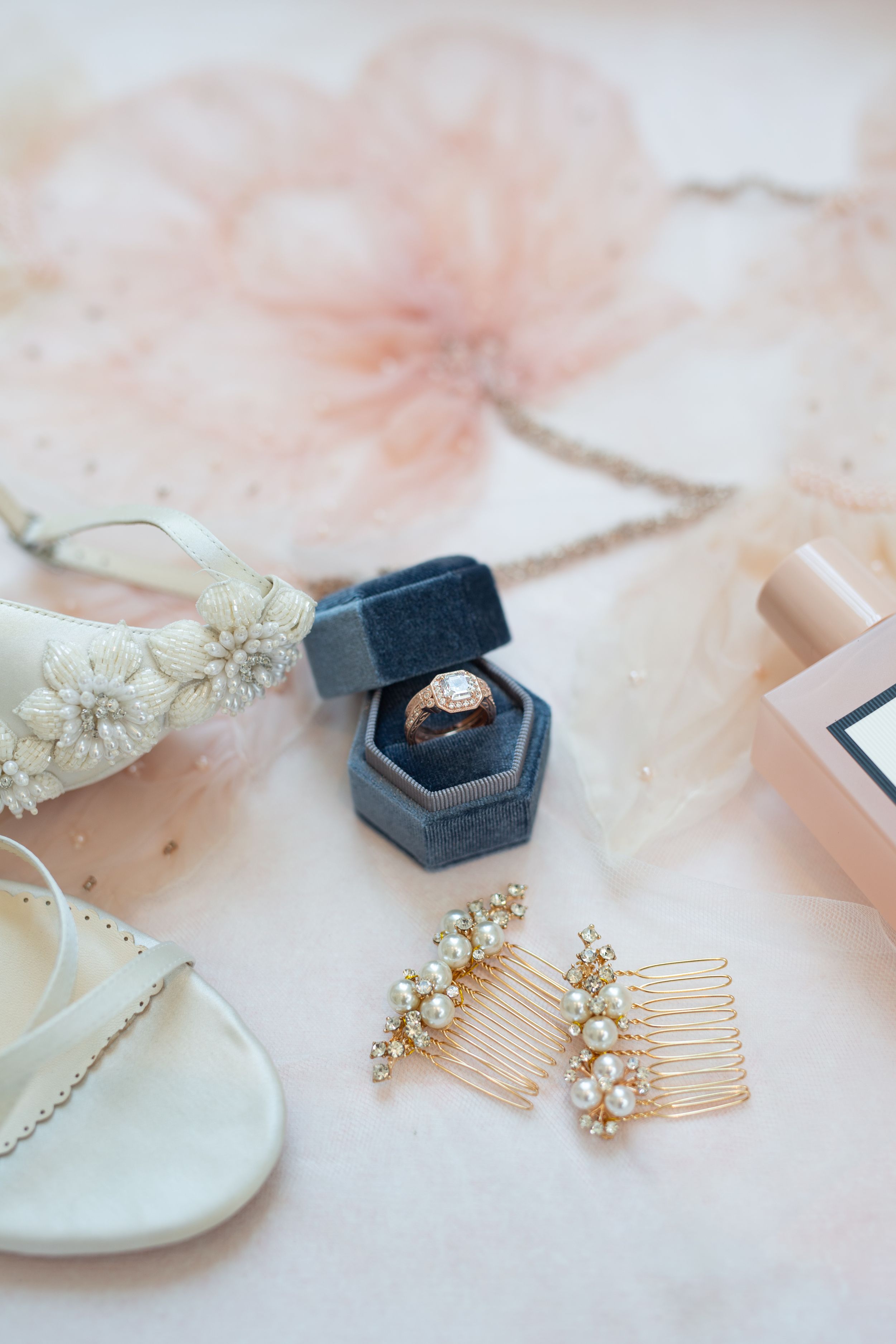 Wedding accessories including blue ring box, hair combs, and delicate jewelry on pink background.