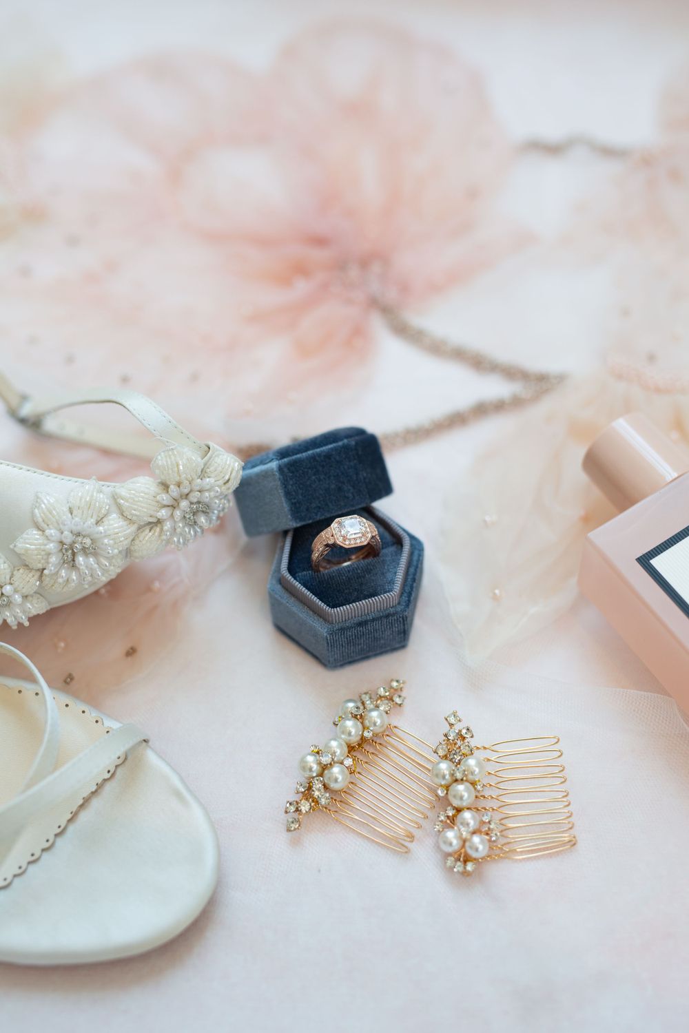 Wedding accessories including blue ring box, hair combs, and delicate jewelry on pink background.