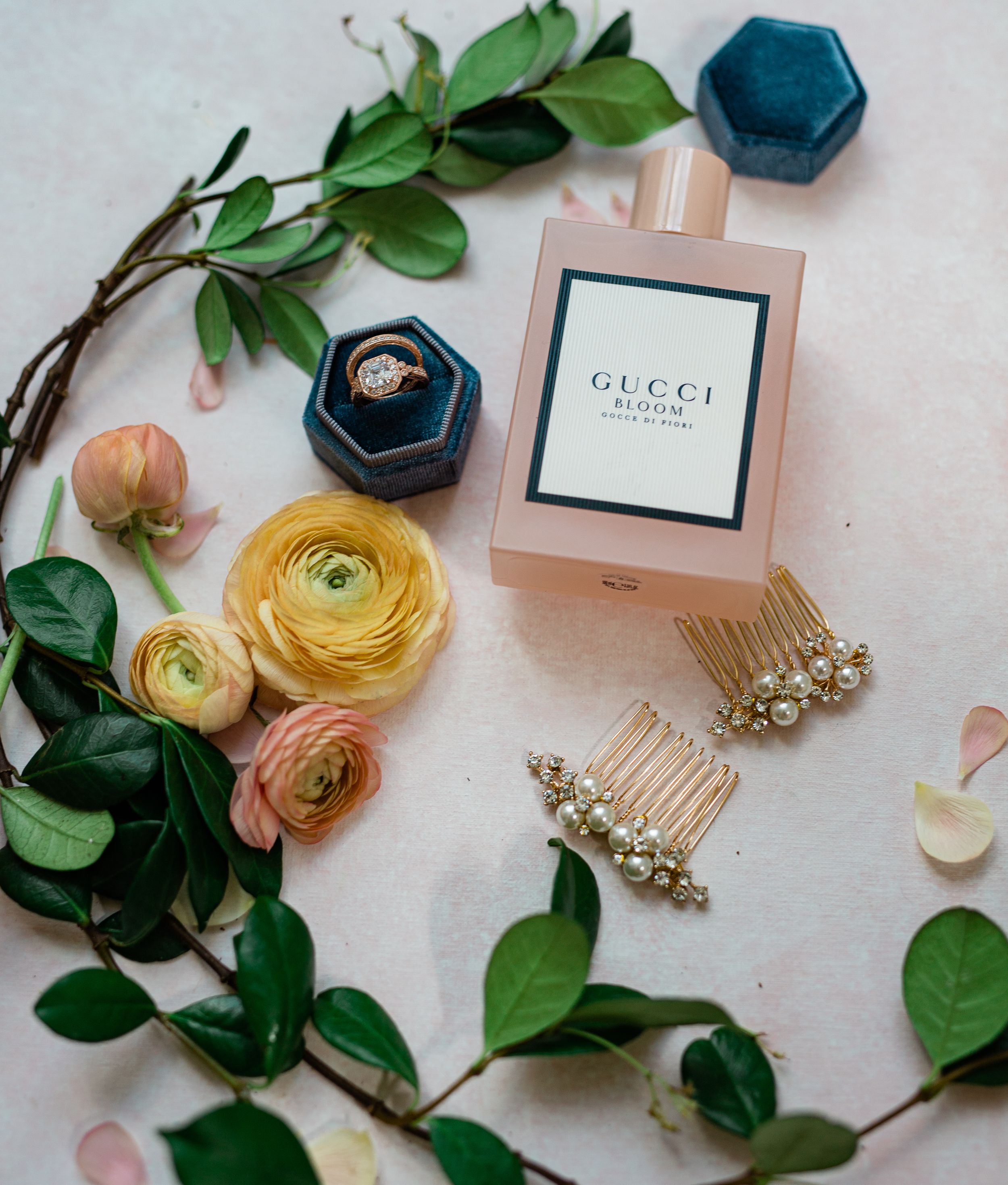Wedding accessories including yellow ranunculus flowers, jewelry, and perfume bottles arranged on a light surface.
