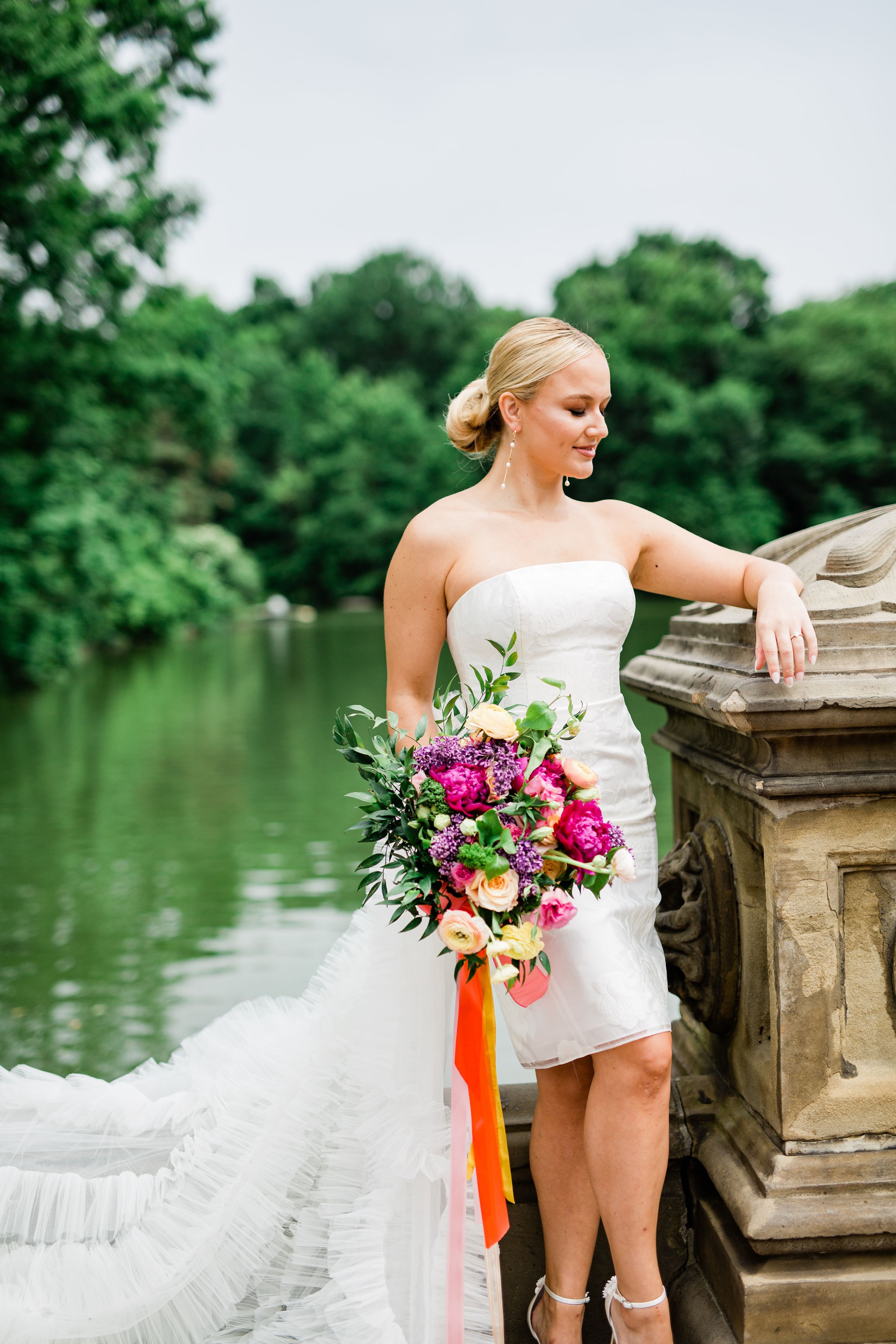 A strapless white wedding gown and vibrant bouquet photographed by a lake.