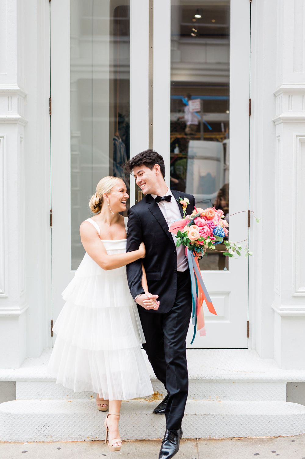 A joyful wedding scene against white architectural columns with soft natural lighting.