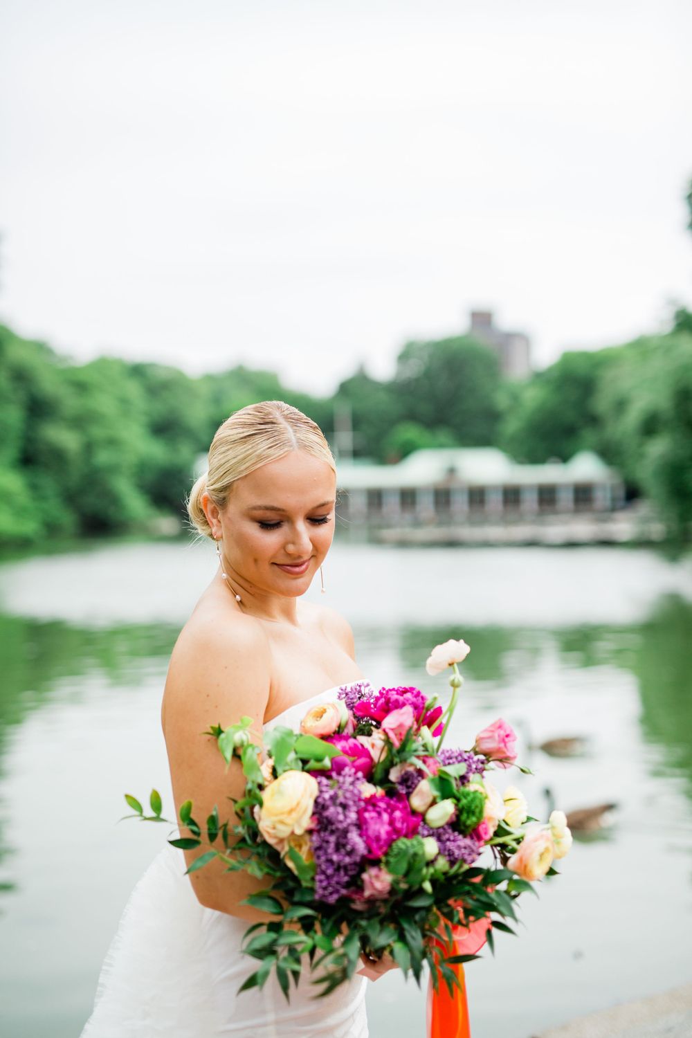 A bright wedding bouquet with pink and purple flowers held near a waterfront setting.