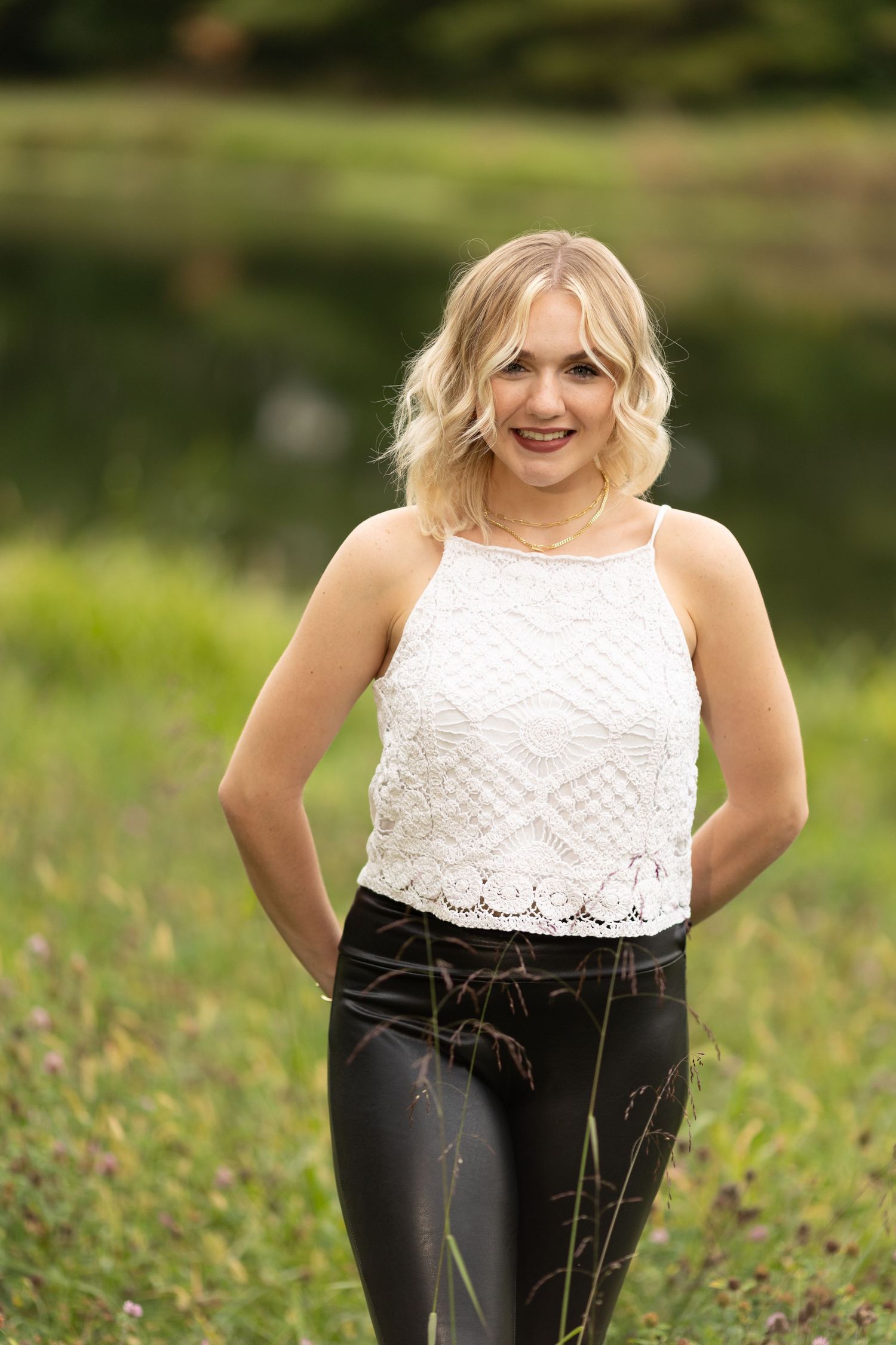 Crochet top and leather pants wearing girl poses demurely in front of countryside pond.
