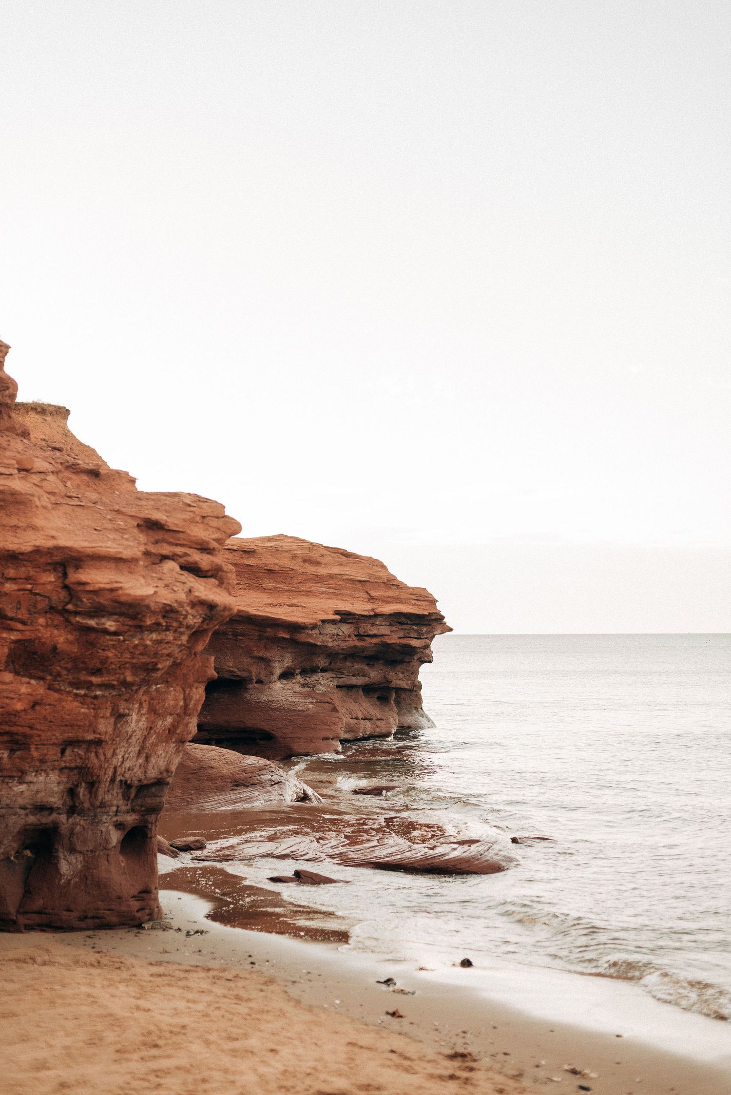 Dramatic red sandstone cliffs overlooking ocean with sandy beach below.