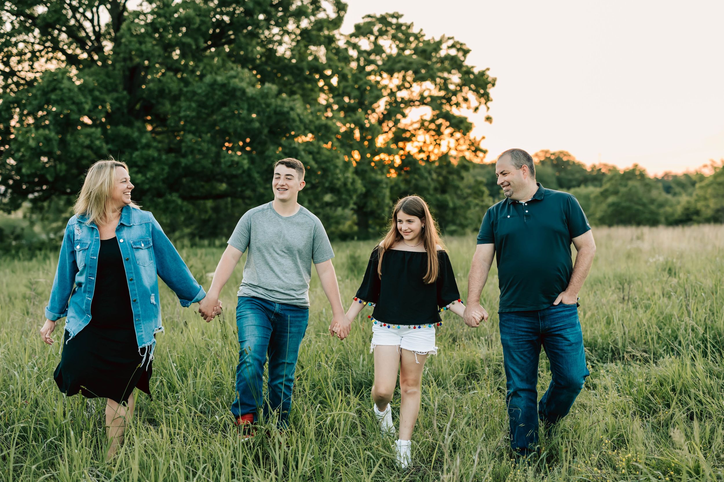 Family walking hand-in-hand through grassy field at sunset.
