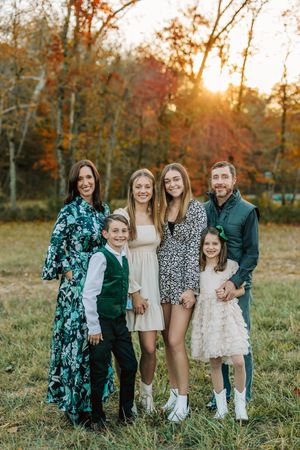 Family of six poses together outdoors during autumn sunset.
