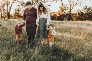 Family of four standing together in tall grass field during golden hour.