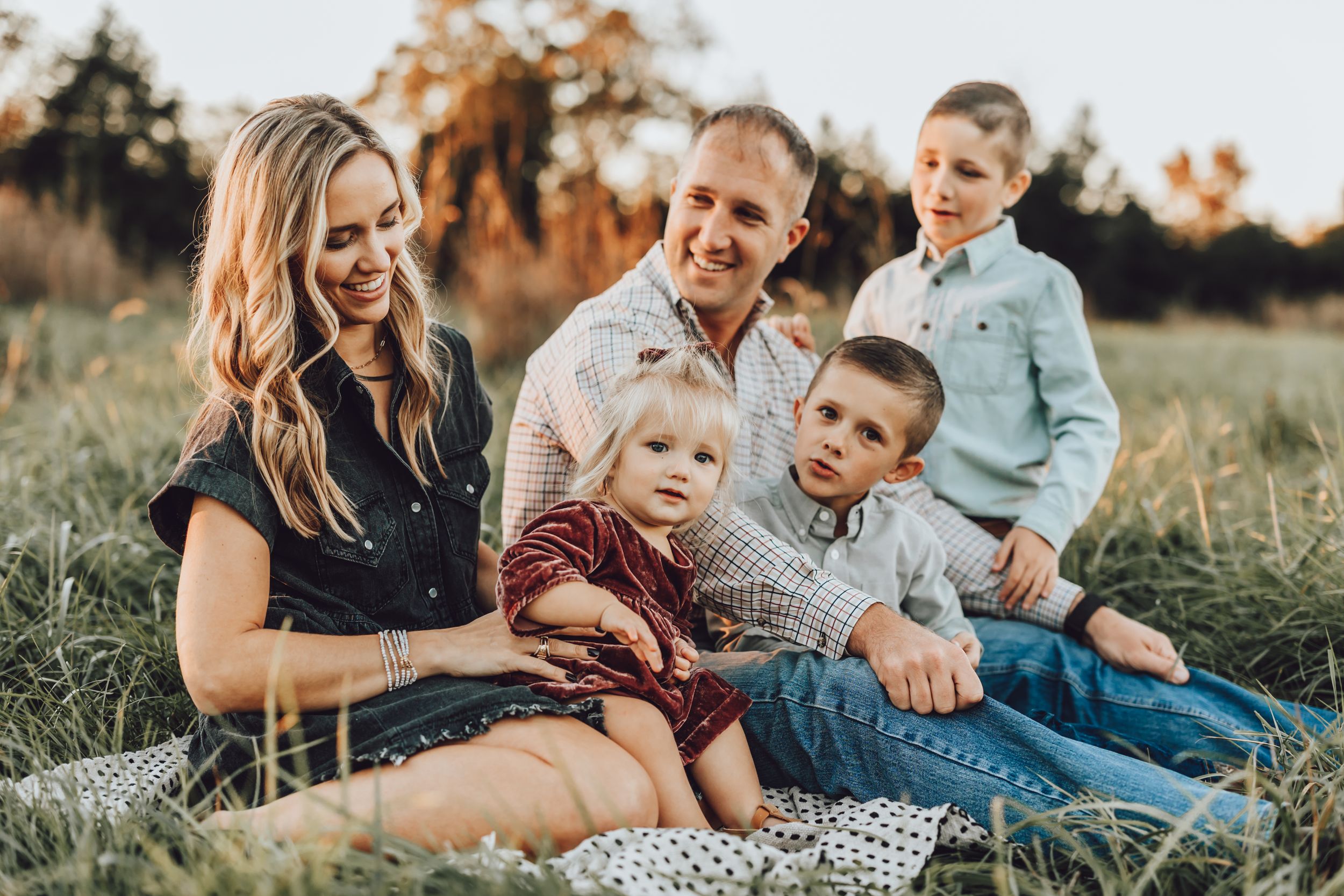 Family relaxing together on picnic blanket in grassy field at sunset.
