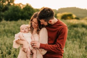 Family shares tender moment with baby in meadow during golden hour.
