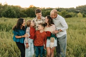 Family sharing playful moment together in tall grass field at sunset.