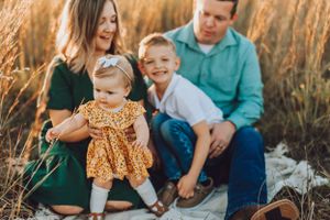 Family sits together in golden field during sunset photoshoot with toddler in yellow dress.