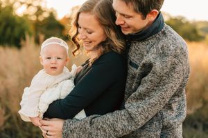 Parents holding baby in warm sweaters during outdoor photo session.