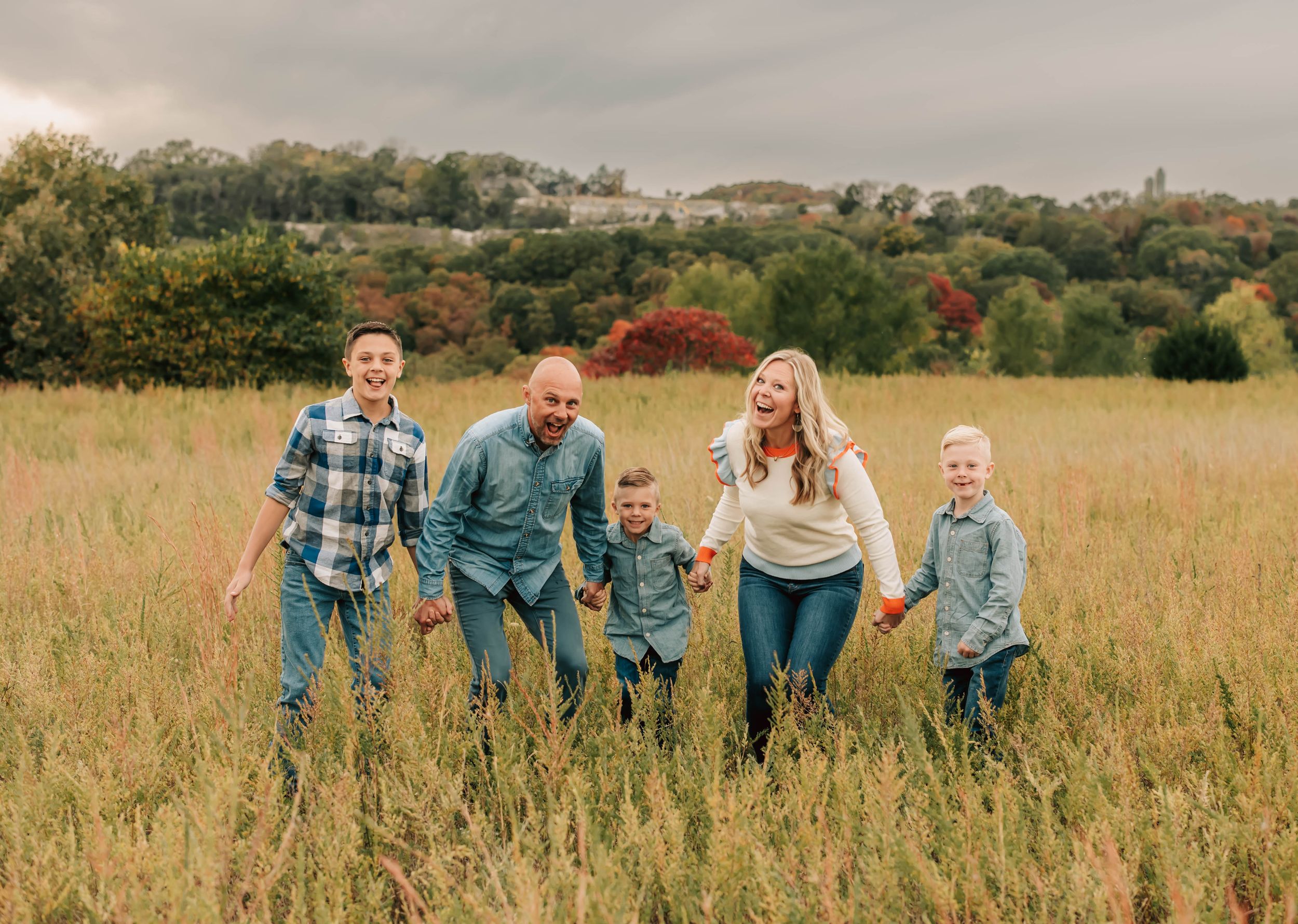 Family of five enjoying a fun moment together in a tall grass meadow during autumn.